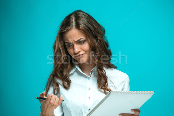 The displeased young business woman with pen and tablet for notes on blue background Stock photo © master1305