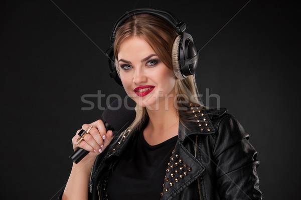 Portrait of a beautiful woman singing into microphone with headphones in studio on black background Stock photo © master1305