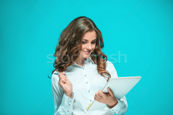 Stock photo: The smiling young business woman with pen and tablet for notes on blue background