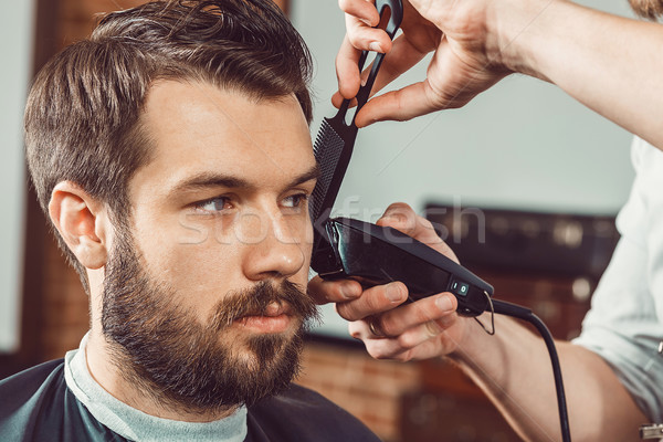 Stock photo: The hands of young barber making haircut attractive man in barbershop