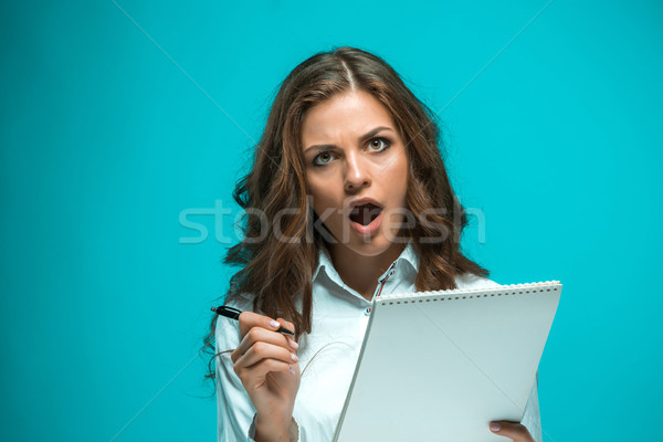 Surprised young business woman with pen and tablet for notes on blue background Stock photo © master1305