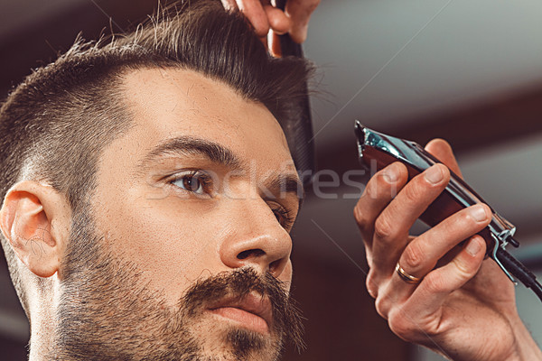 The hands of young barber making haircut to attractive man in barbershop Stock photo © master1305