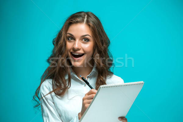 Surprised young business woman with pen and tablet for notes on blue background Stock photo © master1305