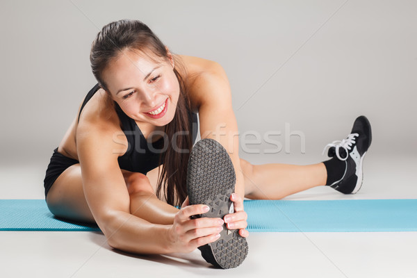 Stock photo: Muscular young woman athlete stretching on gray 