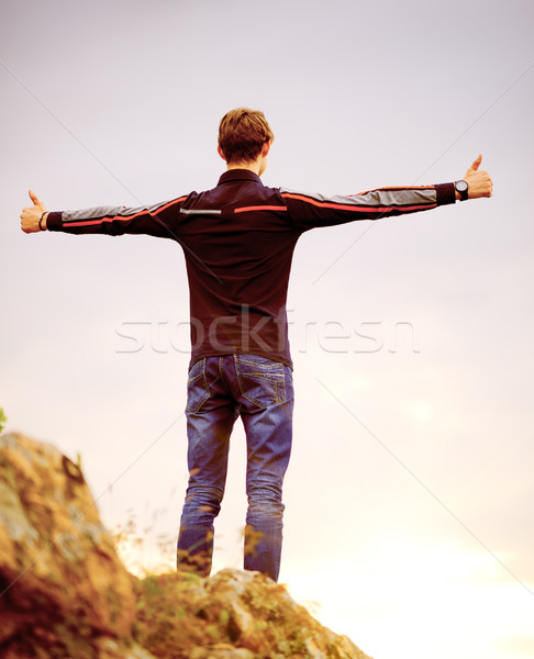 Young Man Standing on Mountain Peak with Arms Raised. Active Lifestyle Concept. Stock photo © maxpro