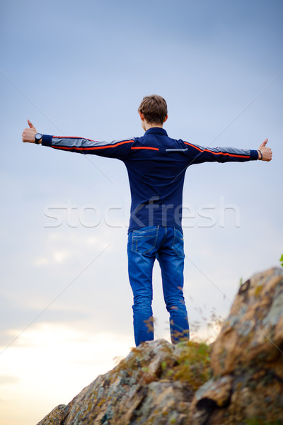Young Man Standing on Mountain Peak with Arms Raised. Active Lifestyle Concept. Stock photo © maxpro