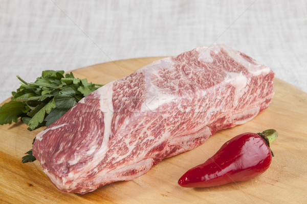 A piece of fresh marbled beef, chili pepper, parsley, ribs lie on a wooden tray Stock photo © mcherevan