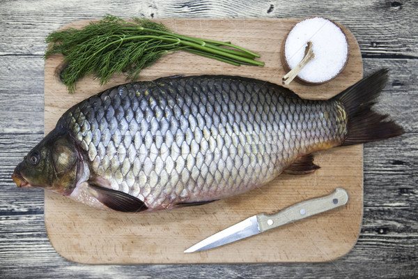 Stock photo: A large fresh carp live fish lying on a wooden board with salt and dill.
