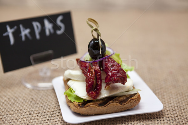 Delicious Spanish tapas, with a rustic mozzarella and dried tomato with olive. TAPAS poster .  Stock photo © mcherevan