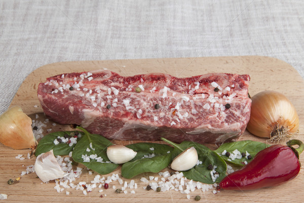 Stock photo: Close-up piece of fresh marbled beef, chili pepper, parsley, onion, garlic, ribs lie on a wooden tra