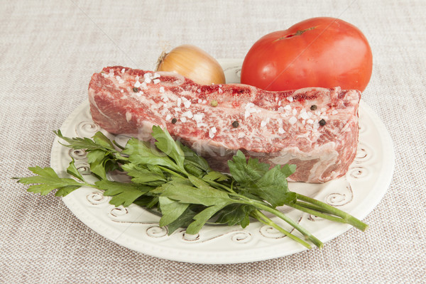 Stock photo: A piece of fresh marbled beef with sea salt and black pepper, tomato, onions on a porcelain plate