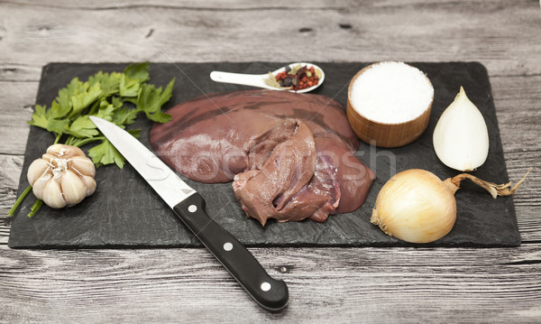 Pieces of fresh raw beef liver, onion, garlic, spices, salt, knife on the stone plate on a white bac Stock photo © mcherevan