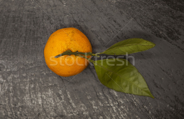 Fresh juicy tasty Sicilian tangerine with a foliage branch on a stone background. Stock photo © mcherevan