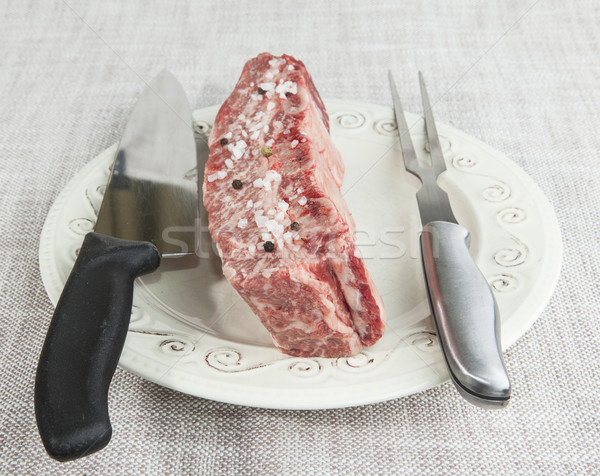 A piece of fresh marbled beef with sea salt and black pepper, knife and fork on a porcelain plate Stock photo © mcherevan