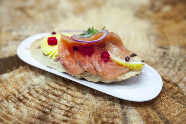 Fresh Spanish tapas on bread baguette smoked Norwegian salmon with black olive butter, herbs and oni Stock photo © mcherevan