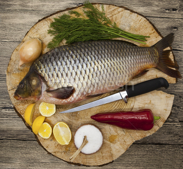 Fresh raw fish carp caught lying on a wooden stump with a knife and slices of lemon and with salt di Stock photo © mcherevan