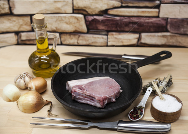 A piece of delicious fresh raw pork close-up on a cast-iron frying pan, onions, garlic, spices, salt Stock photo © mcherevan