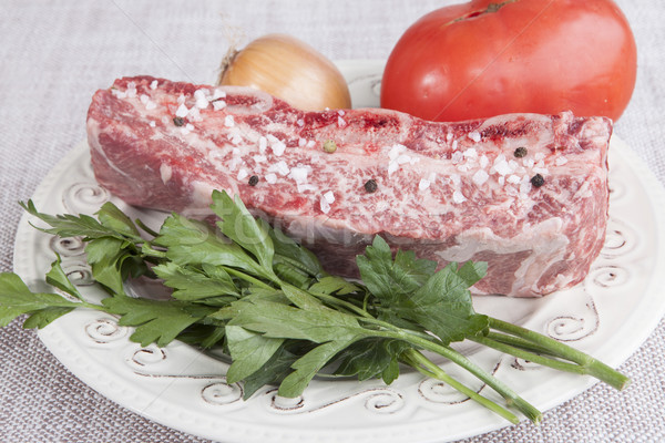 A piece of fresh marbled beef with sea salt and black pepper, tomato, onions on a porcelain plate Stock photo © mcherevan