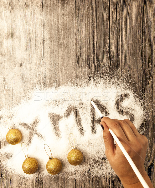 Christmas card with a female hand writing xmas, gold balls in the snow on a wooden background. Stock photo © mcherevan