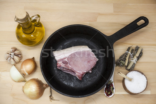 A piece of delicious fresh raw pork close-up on a cast-iron frying pan, onions, garlic, spices, salt Stock photo © mcherevan