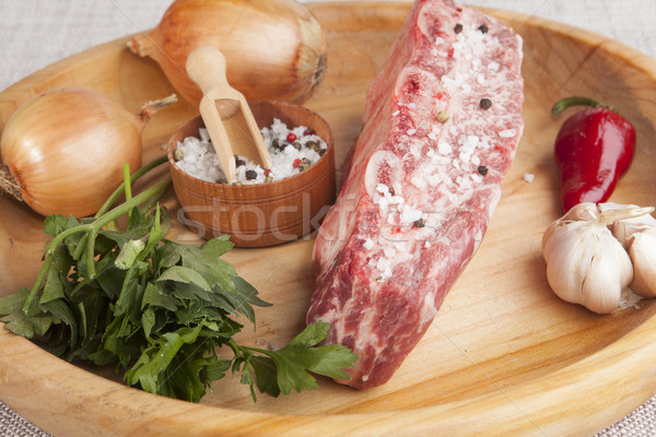 Stock photo: A piece of fresh marbled beef, chili pepper, parsley, onion, garlic, ribs lie on a wooden tray