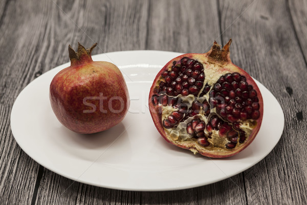 Pomegranates have broken into pieces with red berries on a porcelain plate on a dark background. Stock photo © mcherevan