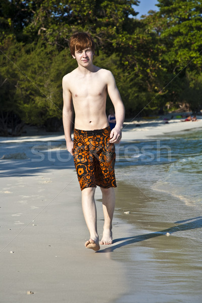 Stock photo: boy with red hair in bathing cloths is walking on a beautiful be