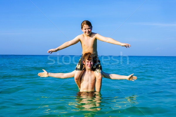 Stock photo: boys having fun playing Piggyback in the warm ocean 