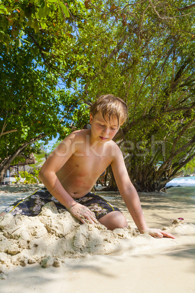 happy young boy is digging in the sand of the beach and construc Stock photo © meinzahn