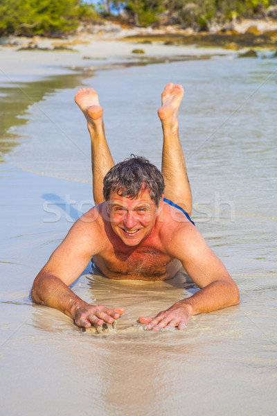 Man in bathingsuit is lying at the beach and enjoying the saltwater with tiny waves and smiles Stock photo © meinzahn