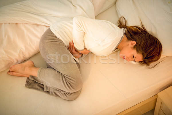 Estômago problema belo mulher jovem cama de mãos dadas Foto stock © MilanMarkovic78