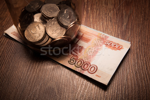Stock photo: Bundle of bank notes and a glass jar with coins