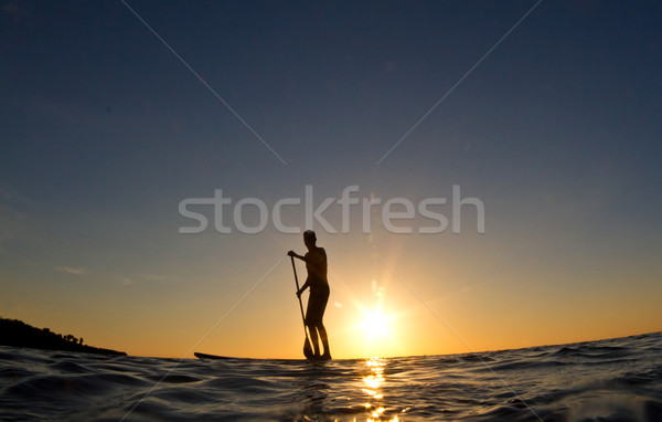 Silhouette of a man paddling his surf board at sunset Stock photo © MojoJojoFoto