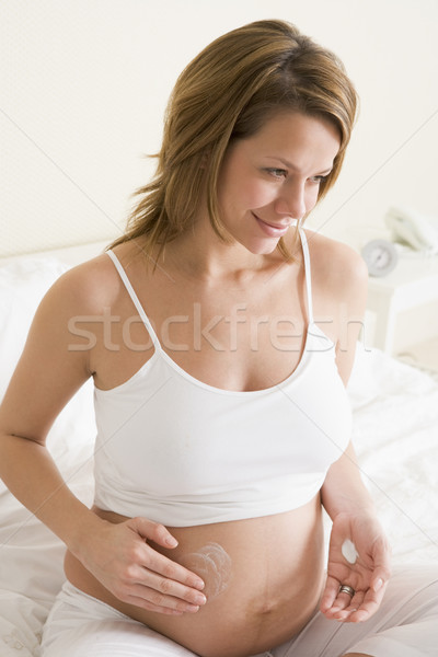 Pregnant woman in bedroom rubbing cream on belly smiling Stock photo © monkey_business
