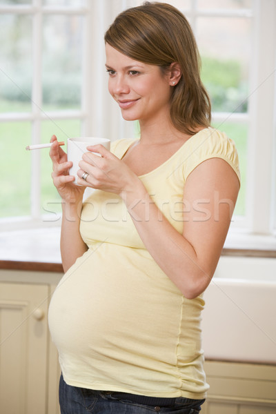 Stock photo: Pregnant woman standing in kitchen with coffee and cigarette smi
