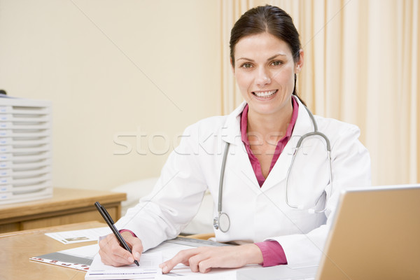Doctor with laptop writing in doctor's office smiling Stock photo © monkey_business