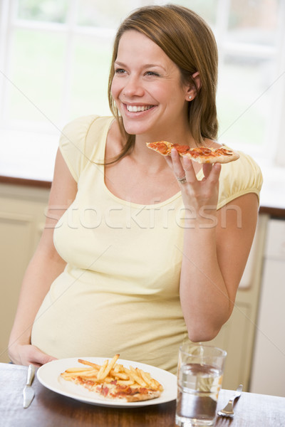 Pregnant woman in kitchen eating French fries and pizza smiling Stock photo © monkey_business