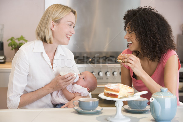 Mother and baby in kitchen with friend eating cake and smiling Stock photo © monkey_business