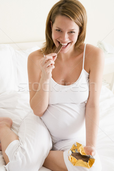 Stock photo: Pregnant woman in bed eating chocolate smiling