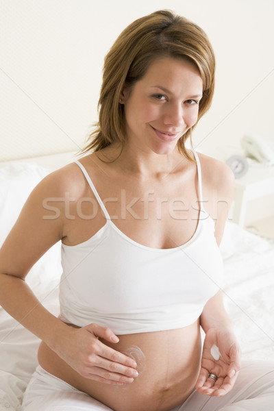 Pregnant woman in bedroom rubbing cream on belly smiling Stock photo © monkey_business