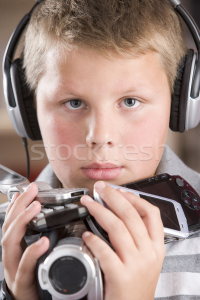Stock photo: Young boy wearing headphones in bedroom holding many electronic 