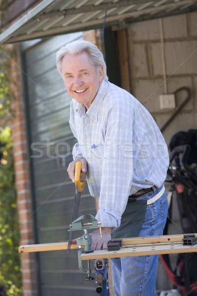 Man at shed sawing wood and smiling Stock photo © monkey_business