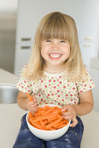 Stock photo: Young girl in kitchen eating carrot sticks smiling