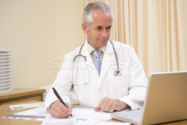Doctor using laptop and writing in doctor's office Stock photo © monkey_business