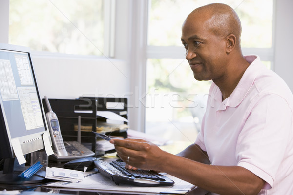 Stock photo: Man in home office using computer holding credit card and smilin