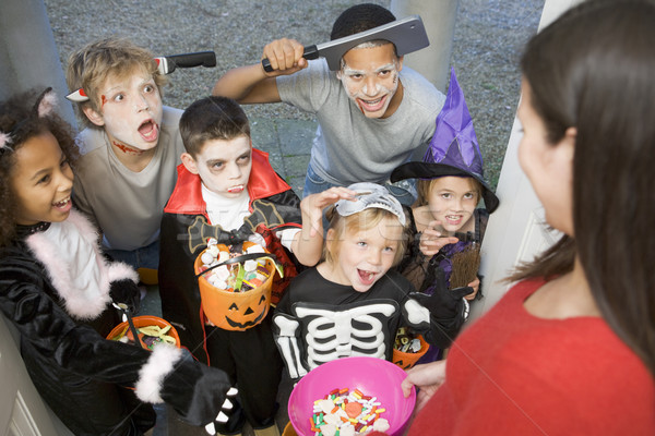 Stock photo: Six children in costumes trick or treating at woman's house