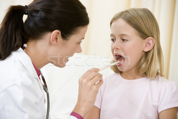 Doctor giving checkup to young girl with tongue depressor in exa Stock photo © monkey_business