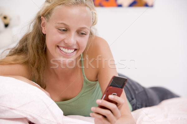 [[stock_photo]]: Adolescente · lit · téléphone · portable · heureux · chambre · souriant