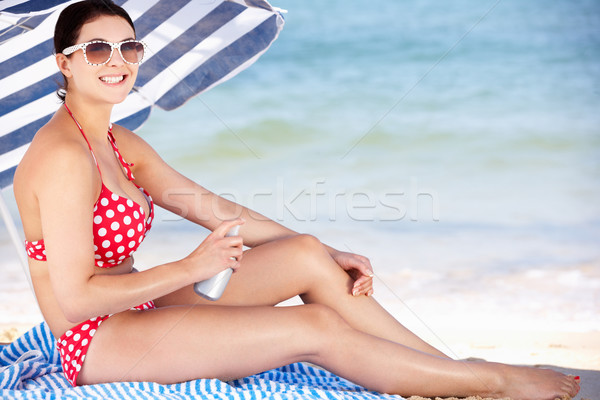 Woman Sheltering From Sun Under Beach Umbrella Putting On Sun Cr Stock photo © monkey_business