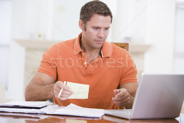 Man in dining room with laptop holding paperwork Stock photo © monkey_business